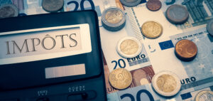 Income tax in France. Calculator with the words « impôts » in French. In the background there are many euro bills and coins. The concept of the need to pay taxes annually