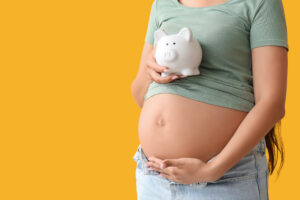 Young pregnant woman with piggy bank on yellow background, closeup. Maternal Benefit concept