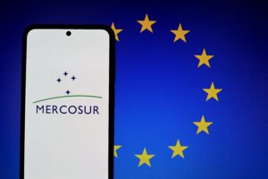 Mercosur and European Union flags. Mercosur logo on a smartphone screen with the European Union flag symbol in the background.