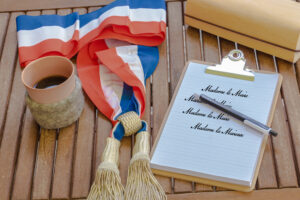 élection municipale en France bloc-note contenant la liste des différentes manières de nommer une femme Maire de sa commune posé sur un bureau en bois avec une écharpe tricolore symbole de sa fonction